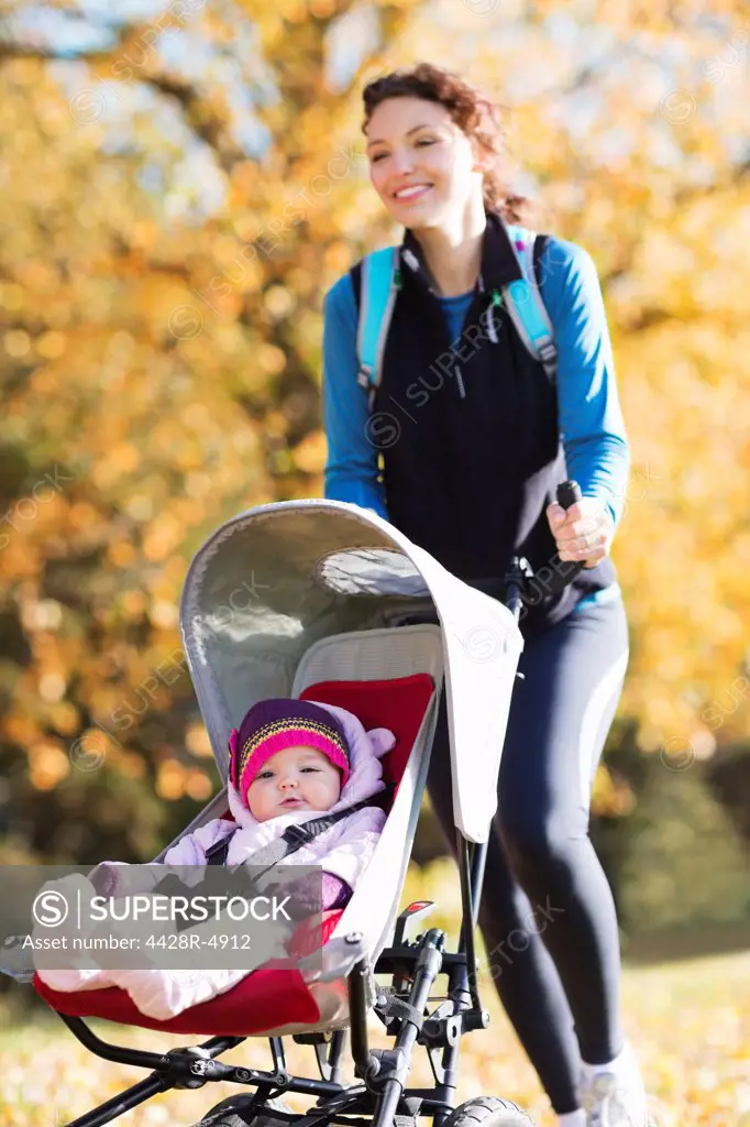 Woman running with baby stroller in park,London, UK