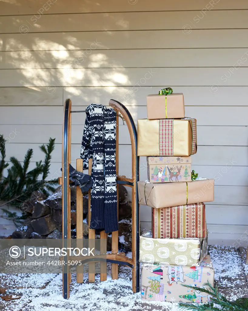 Scarf, wooden sled and Christmas gifts on snowy porch