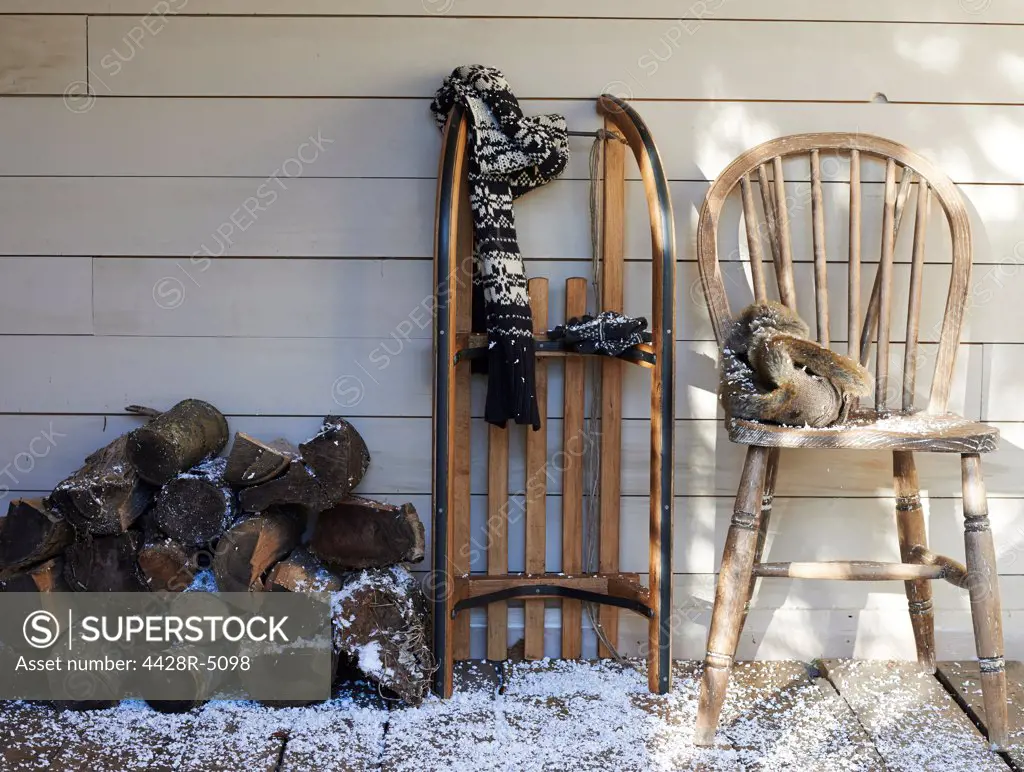 Scarf, wooden sled, chair and firewood on porch