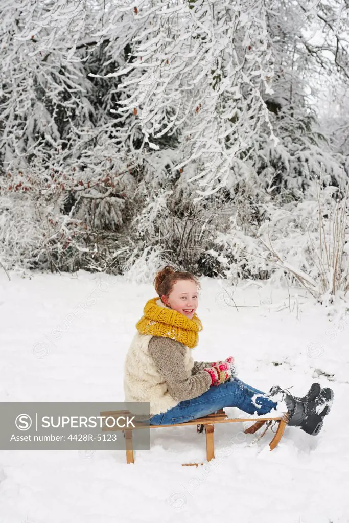 Girl sitting on wooden sled in snow