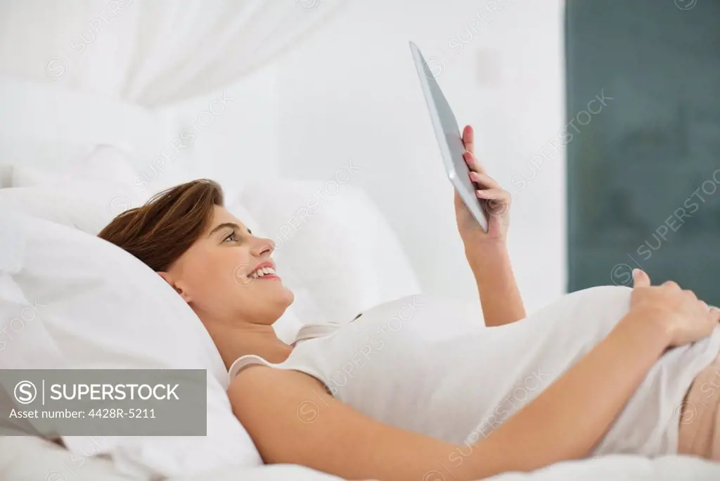 Pregnant woman using tablet computer on bed
