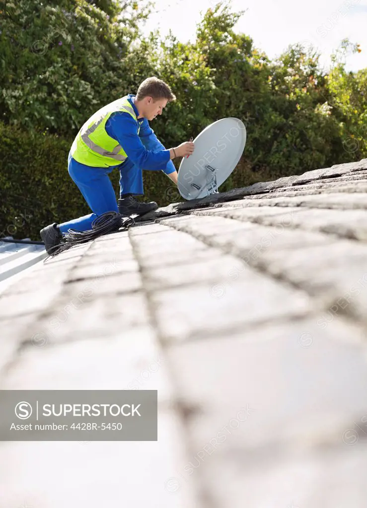 Worker installing satellite dish on roof