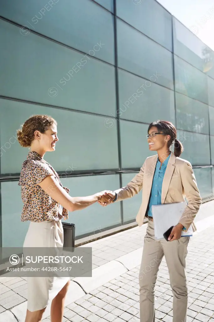 Businesswomen shaking hands on city street