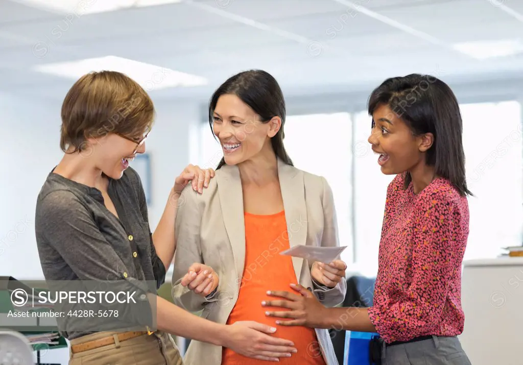 Colleagues admiring pregnant businesswomans belly