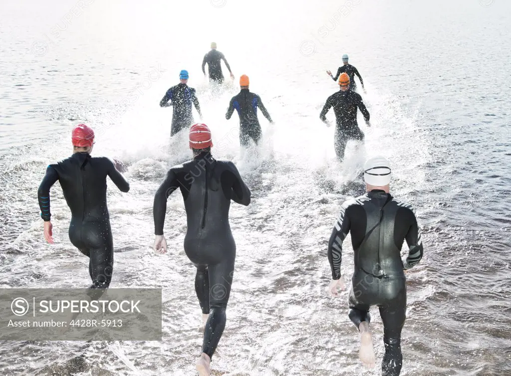 Triathletes in wetsuits running into ocean