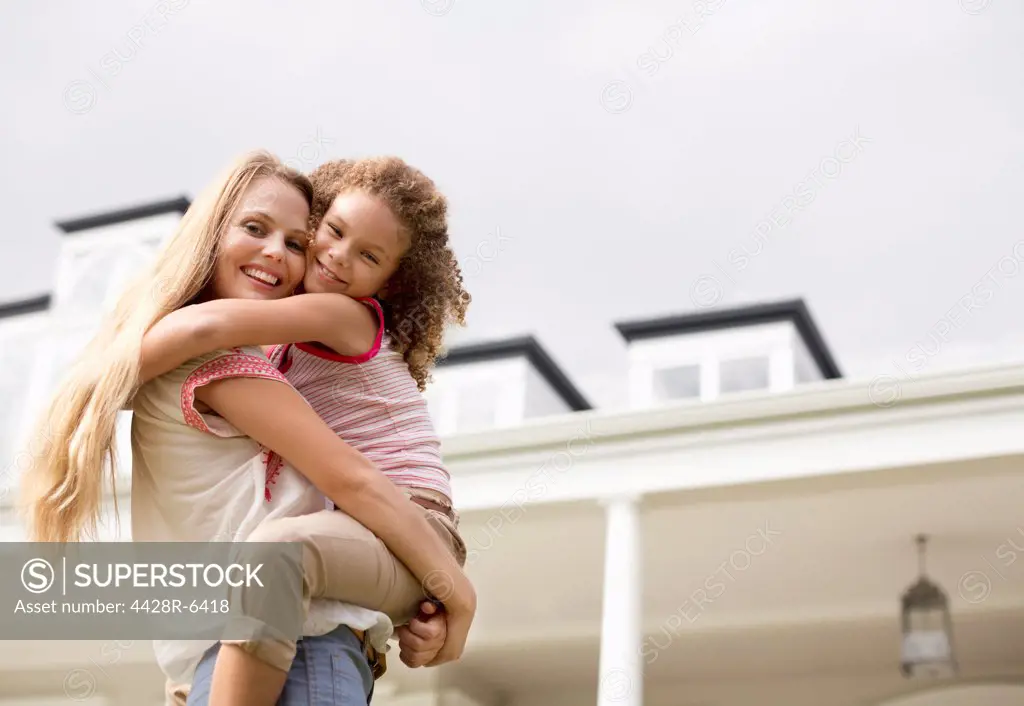 Mother and daughter hugging outside house