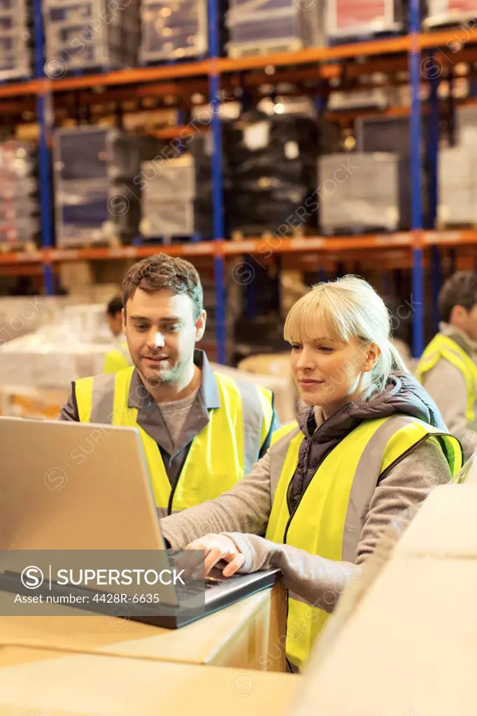 Workers using laptop in warehouse