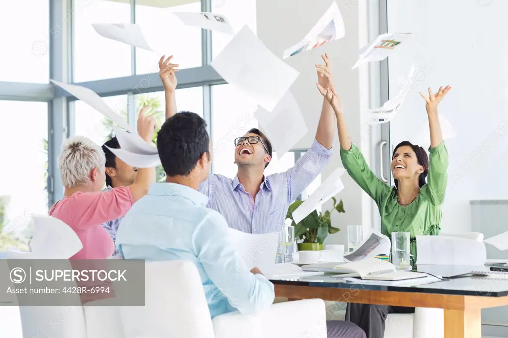 Business people tossing papers in air in meeting