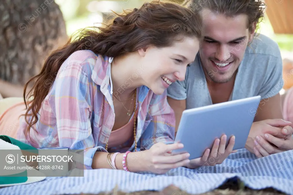 Couple using digital tablet on blanket outdoors
