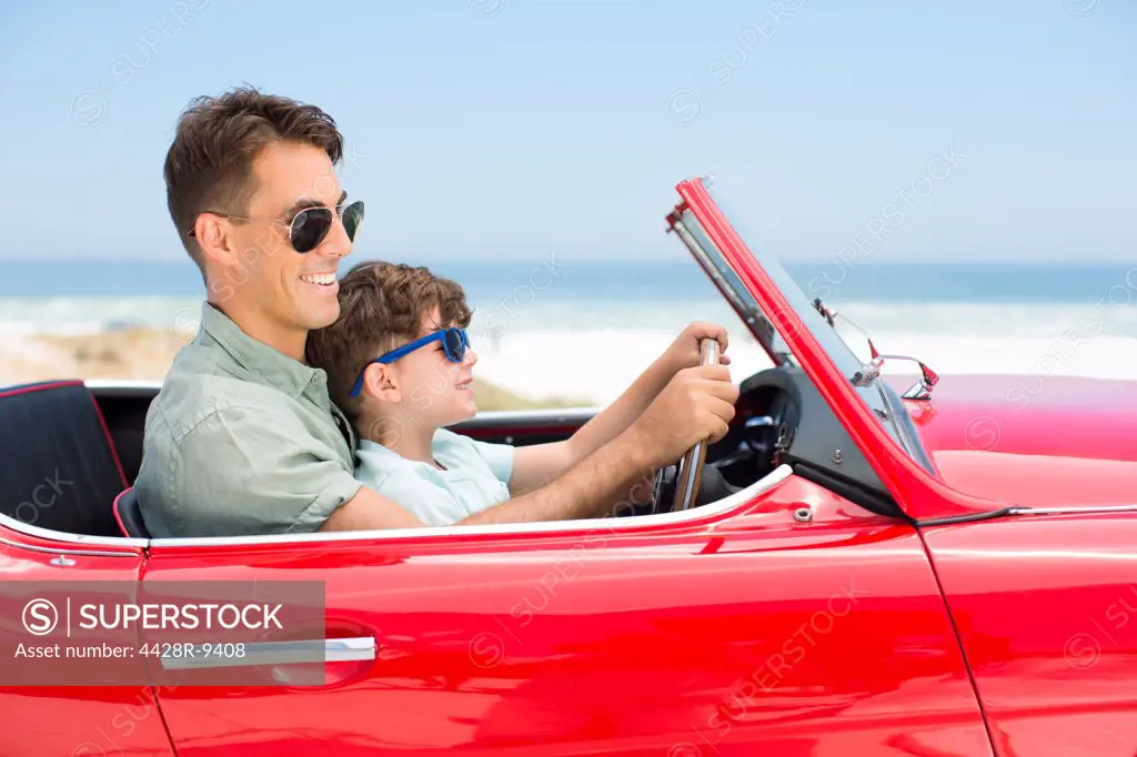 Father and son driving convertible at beach
