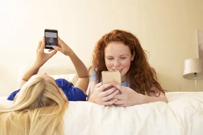 Preteen girl friends using smart phones on bed