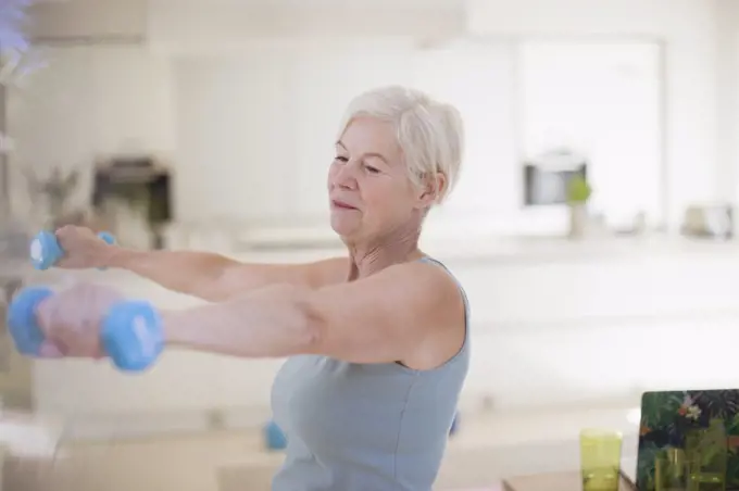 Senior woman exercising with dumbbells in kitchen