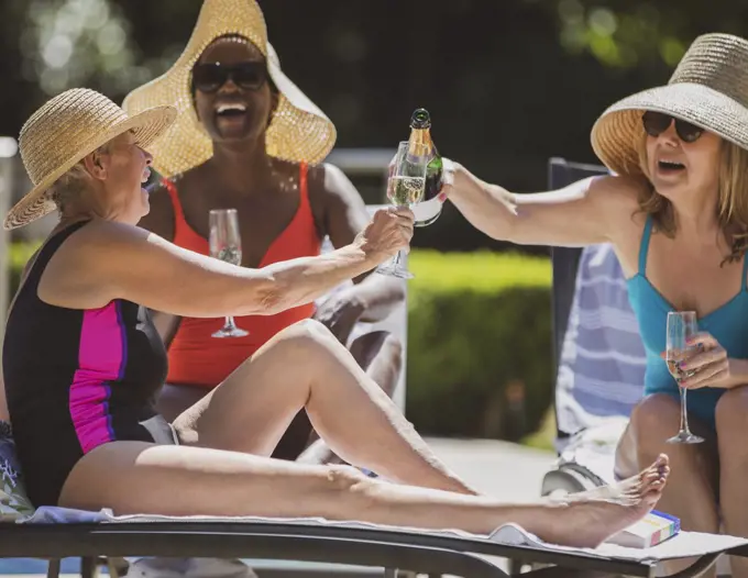 Happy senior women friends drinking champagne on sunny summer patio
