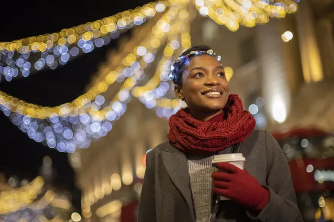 Happy young woman with Christmas light headband in city at night