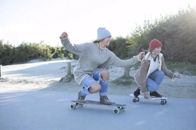 Carefree young women friends skateboarding on beach boardwalk
