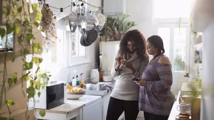 Mother and daughter using smart phones in kitchen