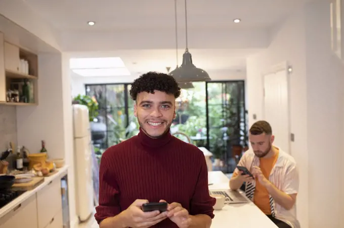 Portrait happy confident young man using smart phone in kitchen