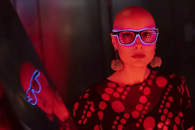 Portrait cool woman with shaved head and neon glasses in red light