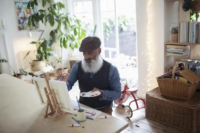 Mature man with beard and palette painting at easel