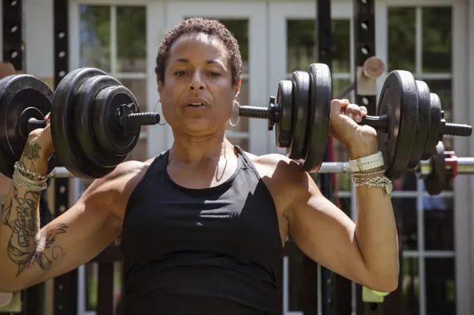 Strong mature woman weightlifting in sunny backyard