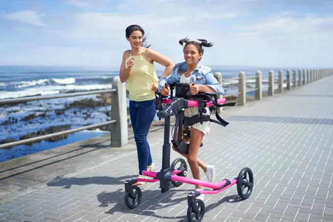 Mother and disabled daughter with rollator jogging on beach boardwalk
