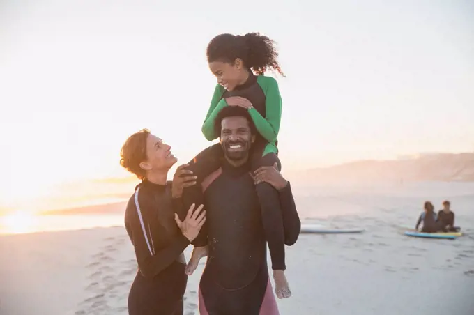 Portrait playful family surfers in wet suits on summer sunset beach