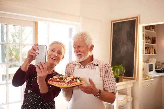 Smiling, confident senior couple taking selfie with pizza at cooking class