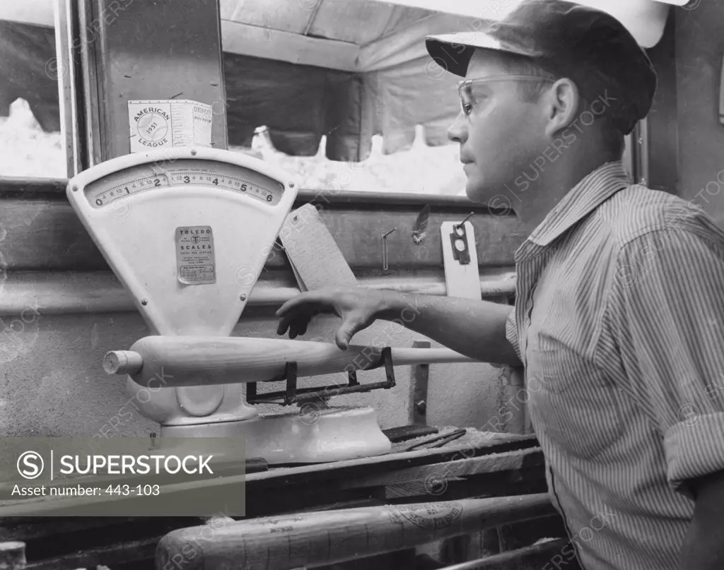 Side profile of a young man weighing a baseball bat in a baseball bat factory, 1951