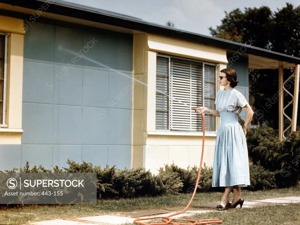 Young woman holding garden hose, spraying house wall, 1948