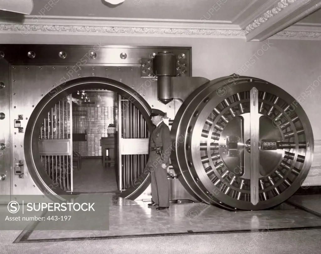 Security guard standing at a bank vault door, 1947