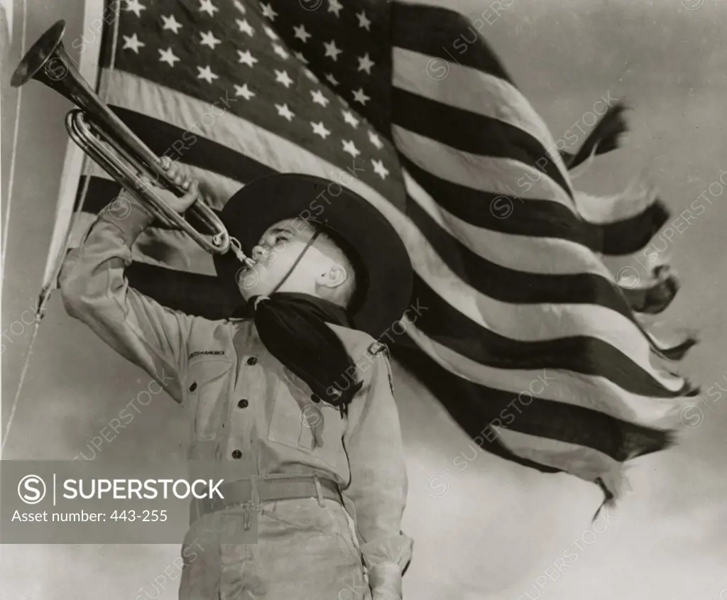 Low angle view of a boy blowing a bugle under an American flag, 1940