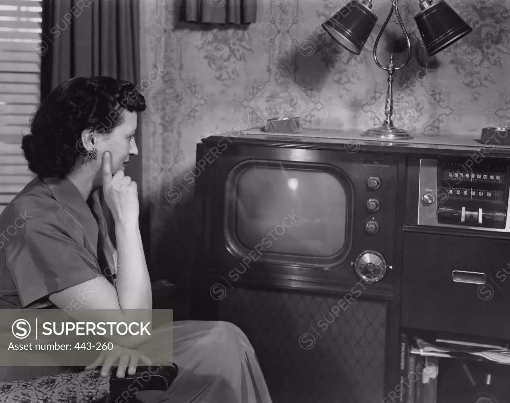 Side profile of a mid adult woman sitting in an armchair in front of a television, 1950