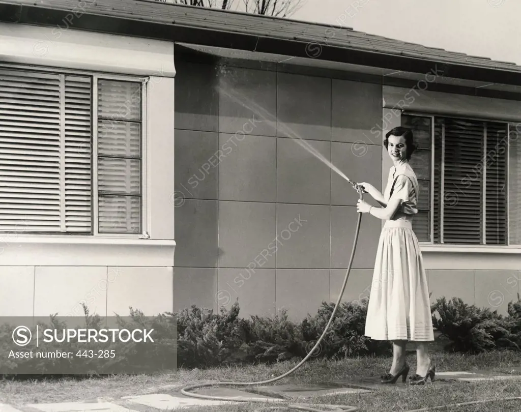 Portrait of a young woman spraying water on the wall of a house