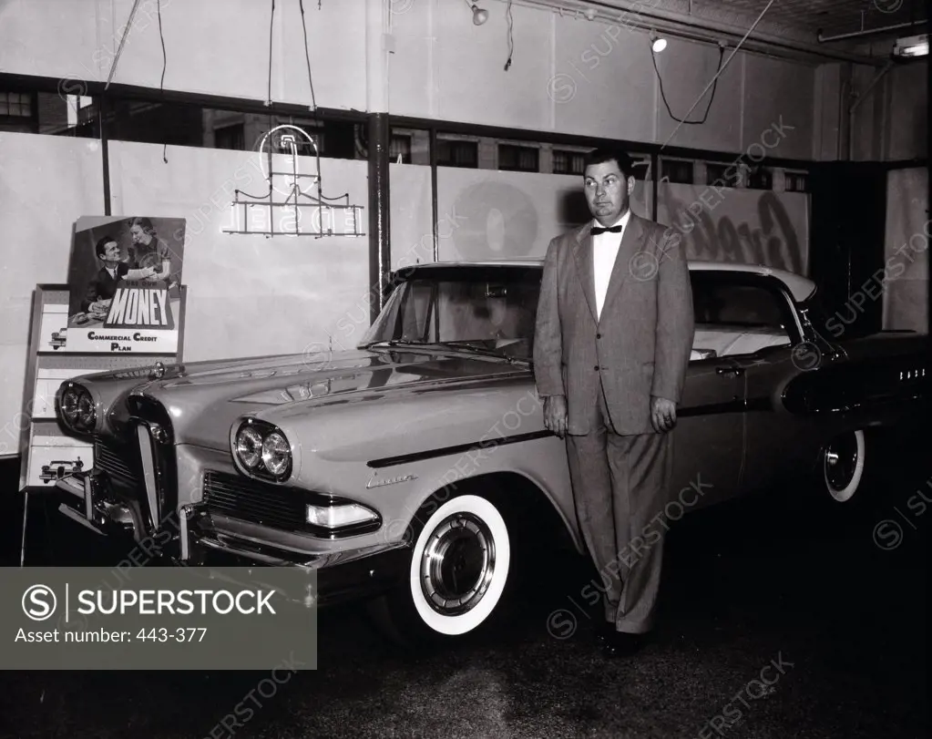 Mature man standing near a car in a showroom, 1958