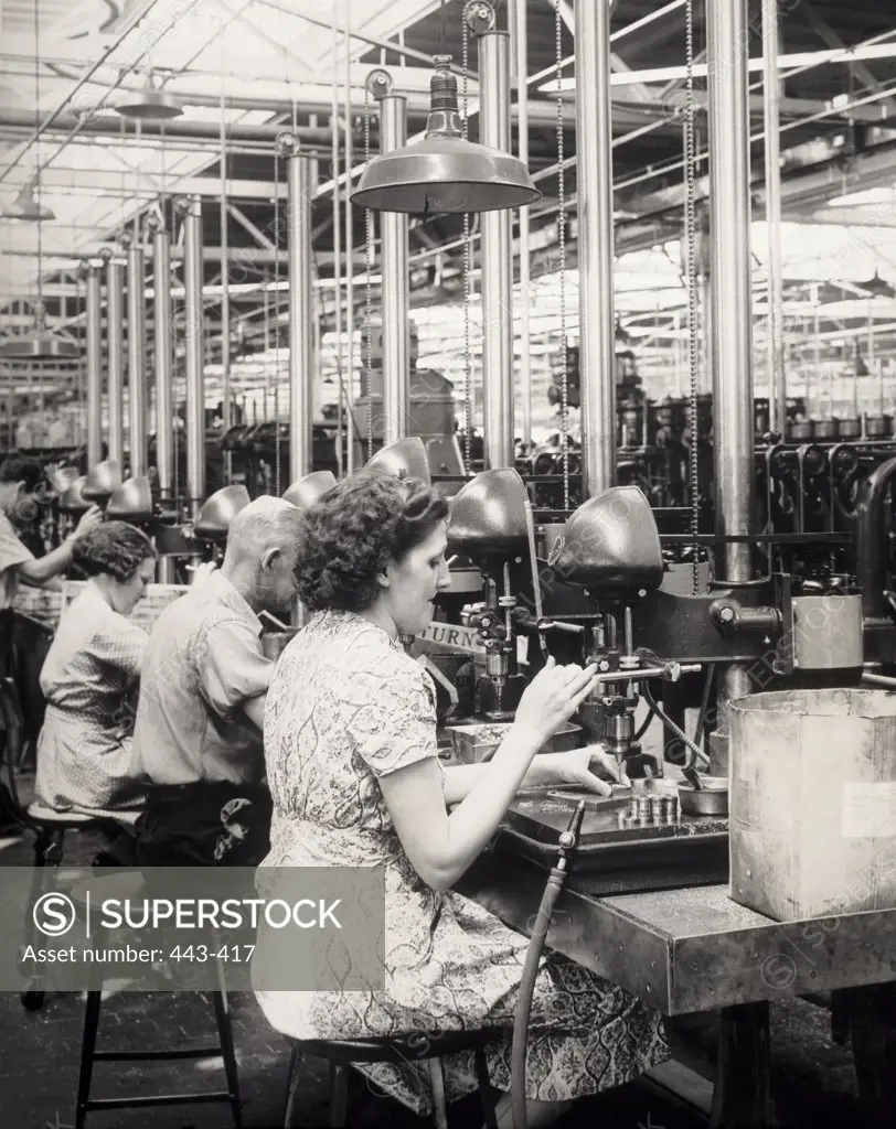 Side profile of four workers operating a drill press in a factory