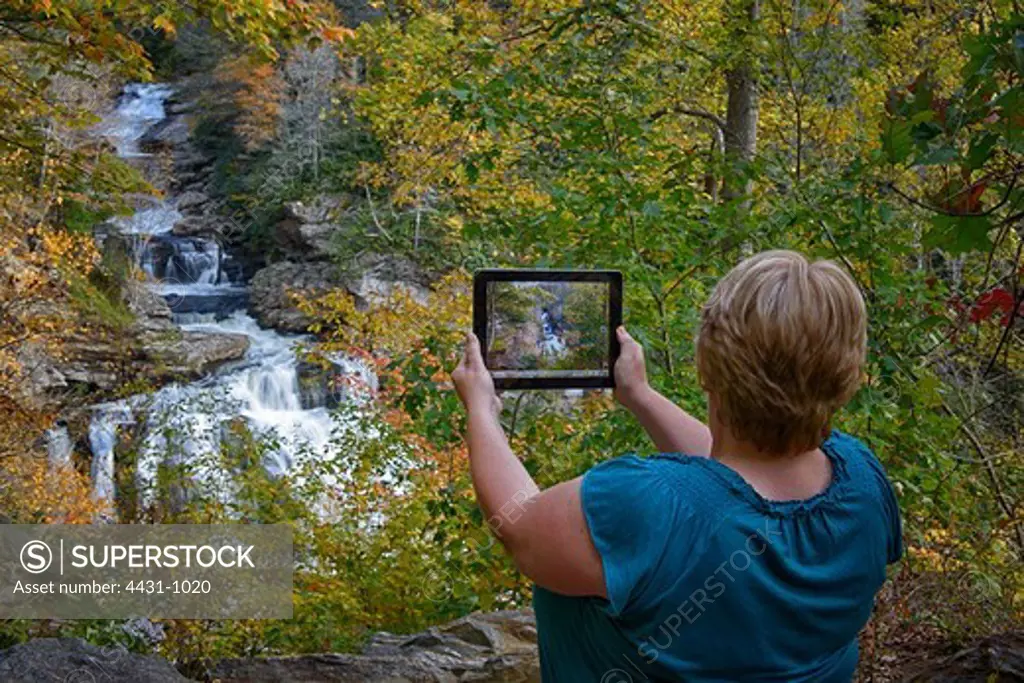 USA, North Carolina, Transylvania County, Dupont State Forest, Woman using tablet to take picture of waterfall in Smoky Mountains