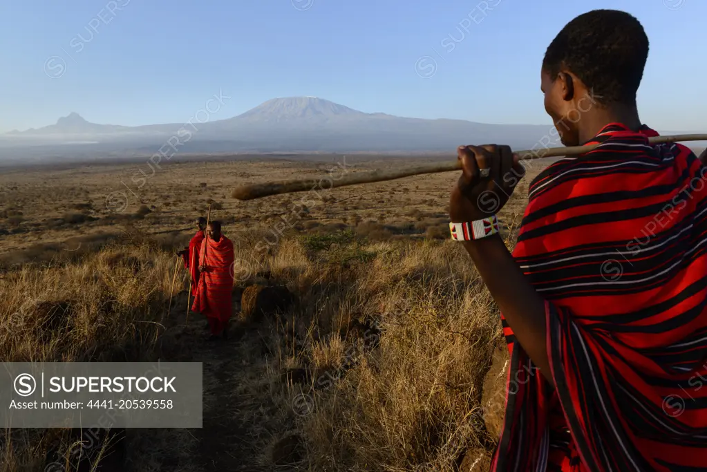 Maasai (Masai) elders with Mount (Mt) Kiliminjaro and Mount (MT)  Mawenzi (in Tanzania) on the left in the background. Satao Elerai Conservancy. Near Amboseli National Park. Kenya.