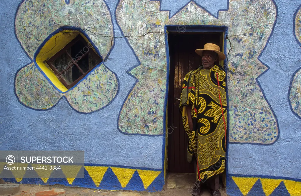 Elderly man standing on door of colourful home, South Africa.