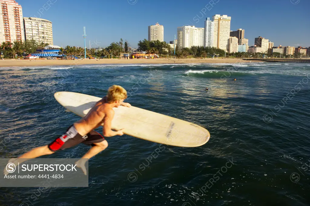 A surfer jumps into the sea from a quay with 'The Golden Mile' in the background.Durban. KwaZulu-Natal, South Africa.