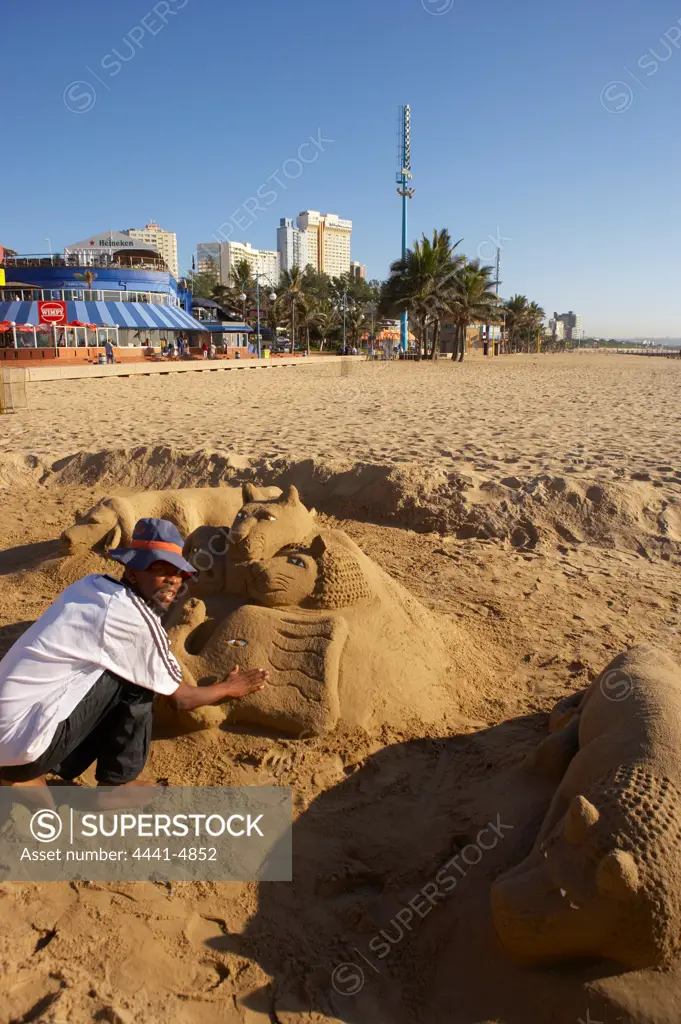 A sand scultptor poses next to his work on the beach front. Durban. KwaZulu-Natal, South Africa.