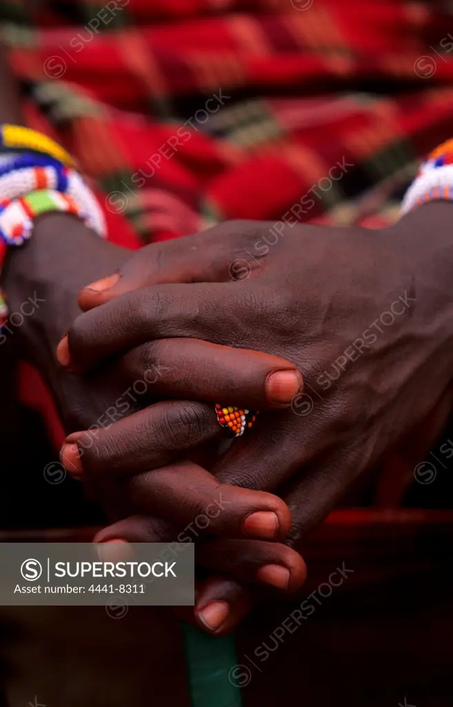 The folded hands of a Maasai warrior. The warriors love brightly coloured jewellery. Olonana village. Maasailand. Kenya.