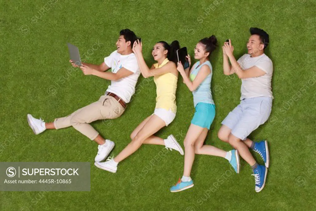 Young people lying on grass looking at phone and tablet