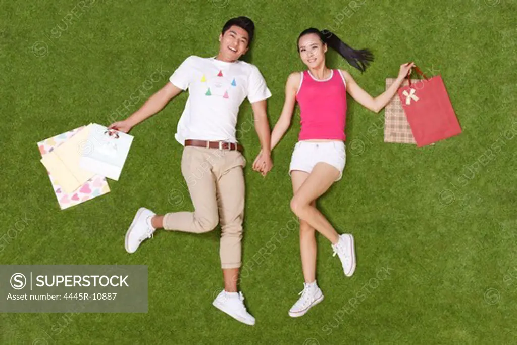 Young couple holding shopping bags lying on grass