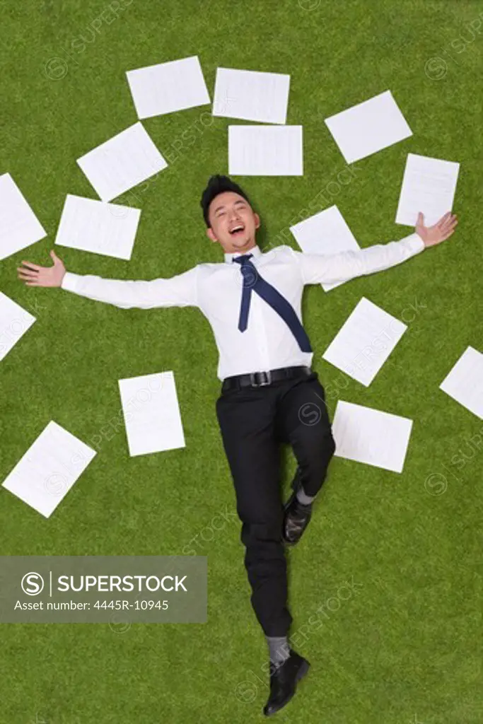 Young man lying on grass with sheets of paper