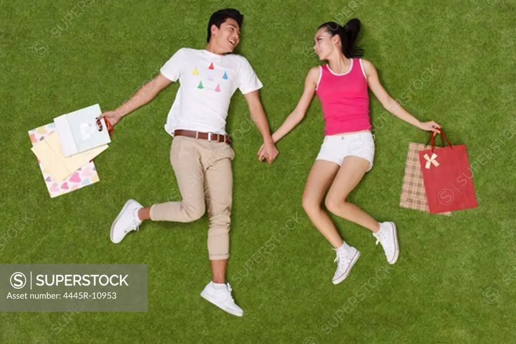 Young couple holding shopping bags lying on grass