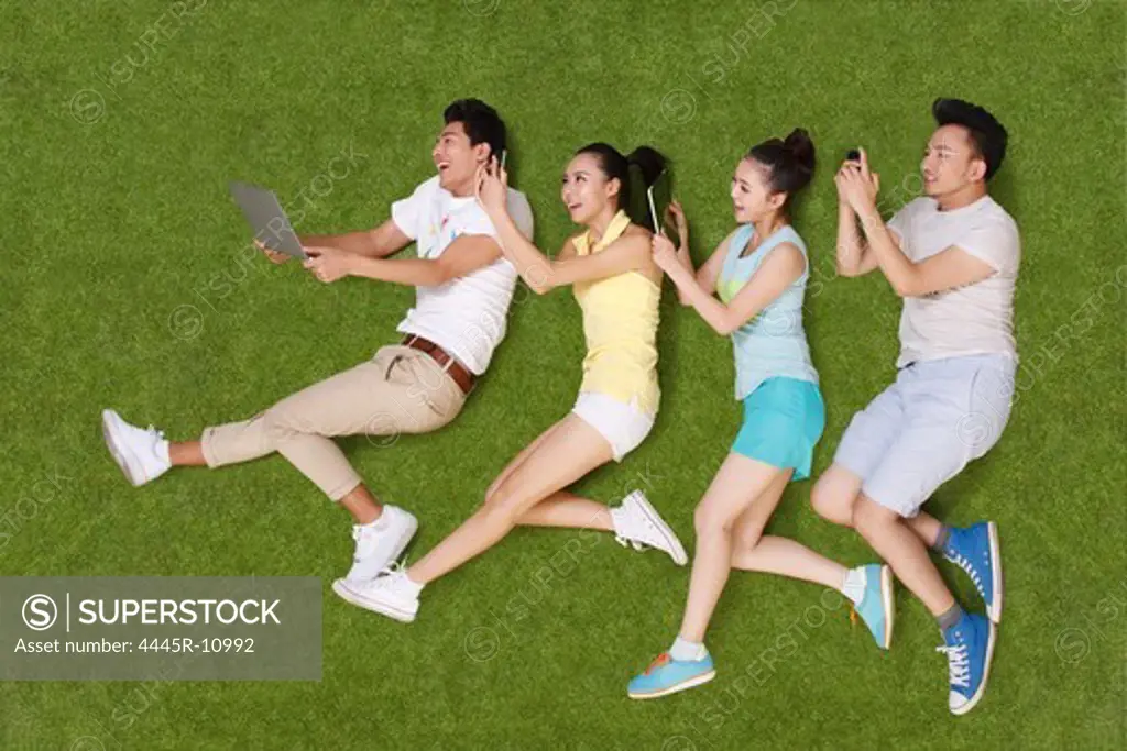Young people lying on grass looking at phone and tablet
