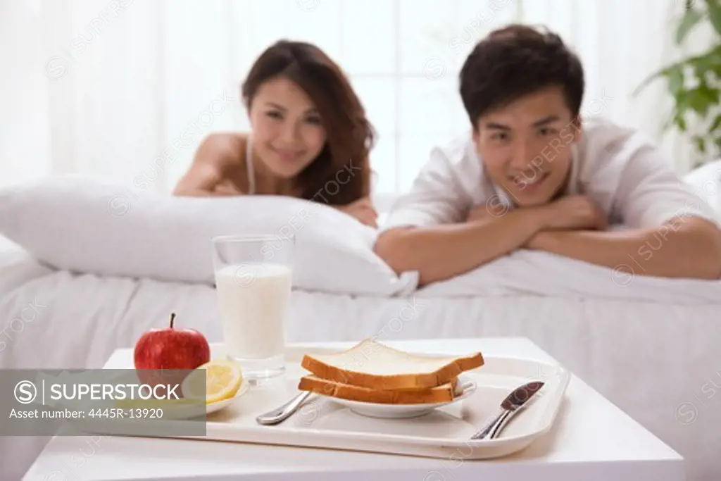 Young couple lying on bed and looking at breakfast