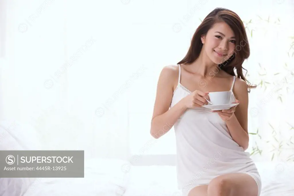 Young lady drinking coffee on bed