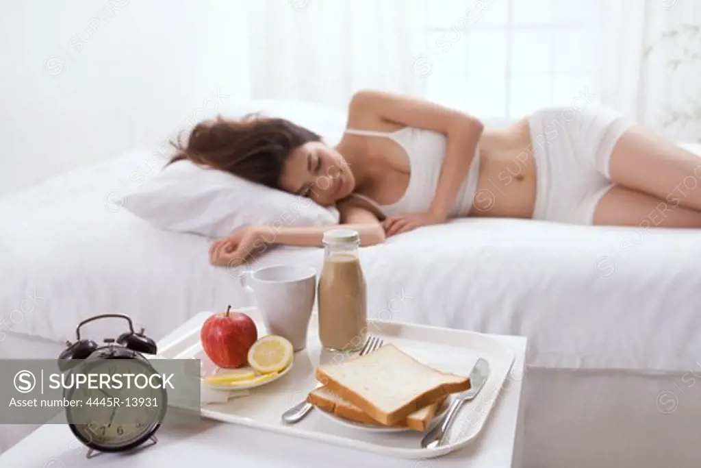 Young lady lying on bed beside breakfast
