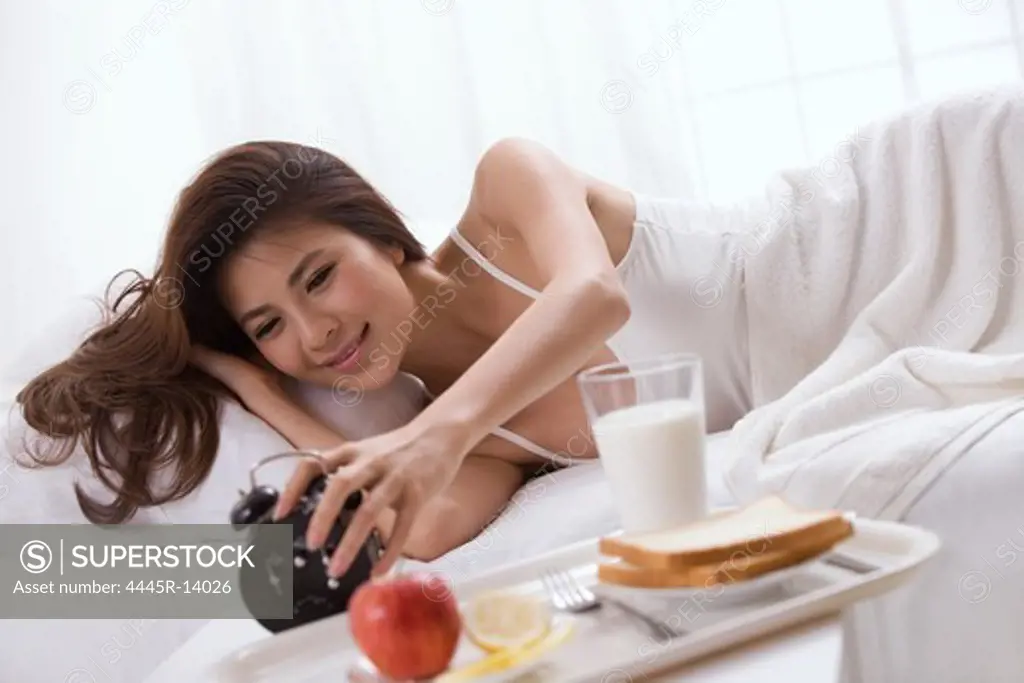 Young lady touching alarm clock on bed